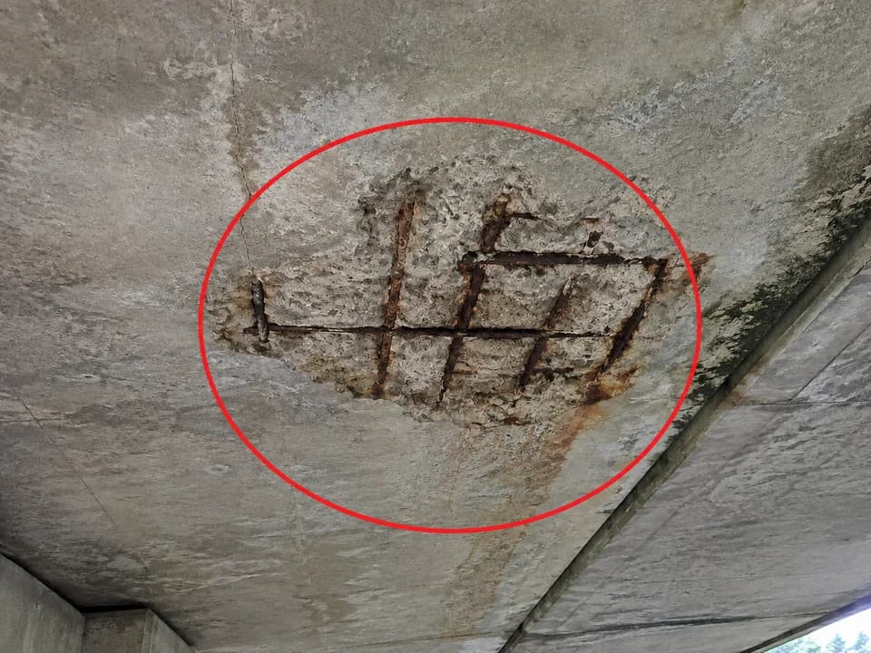 Concrete deck spall with exposed reinforcing steel circled in red